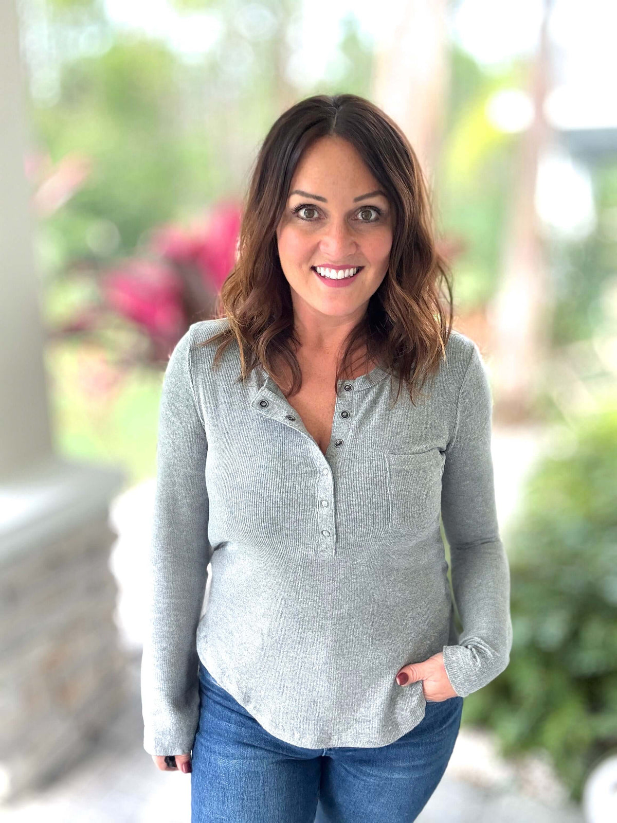 Woman wearing a gray ribbed top with front pocket, standing outdoors.