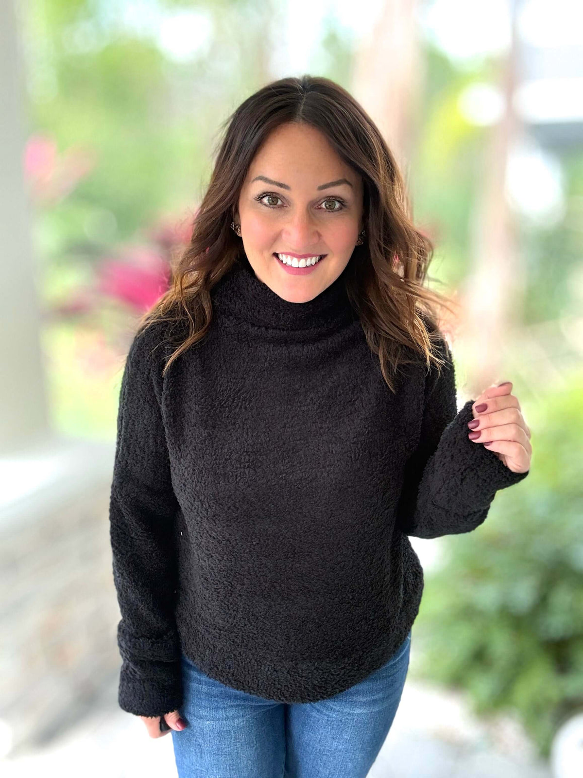 Woman wearing black fuzzy cozy pullover with jeans, showcasing a chic and comfortable look in a natural setting.