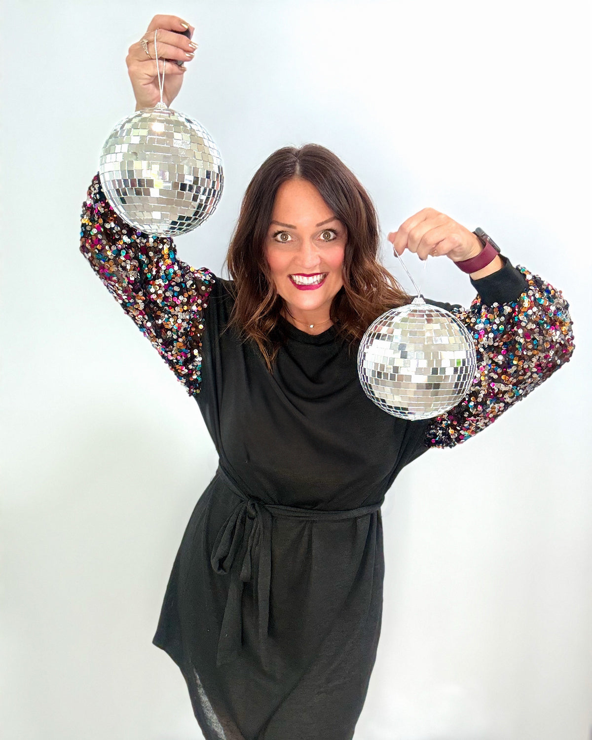 Woman in black dress with sequin sleeves holding disco balls, showcasing the Take Me to the Disco Dress for party occasions.