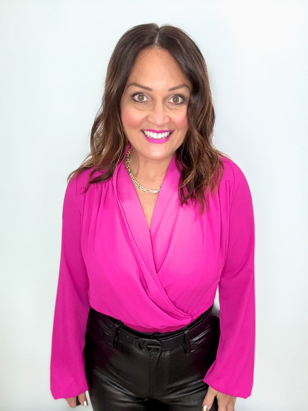 Woman wearing a hot pink bodysuit and black pants, smiling confidently.