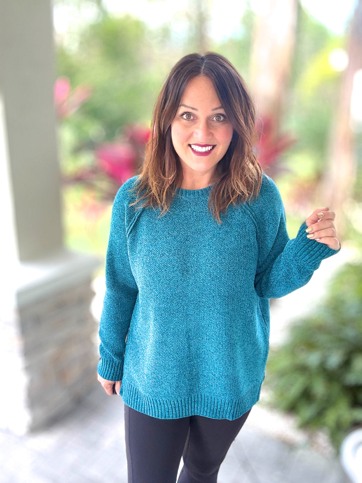 Woman wearing a blue Chenille Dream Sweater with raglan sleeves and round neck, standing outside with greenery in the background.