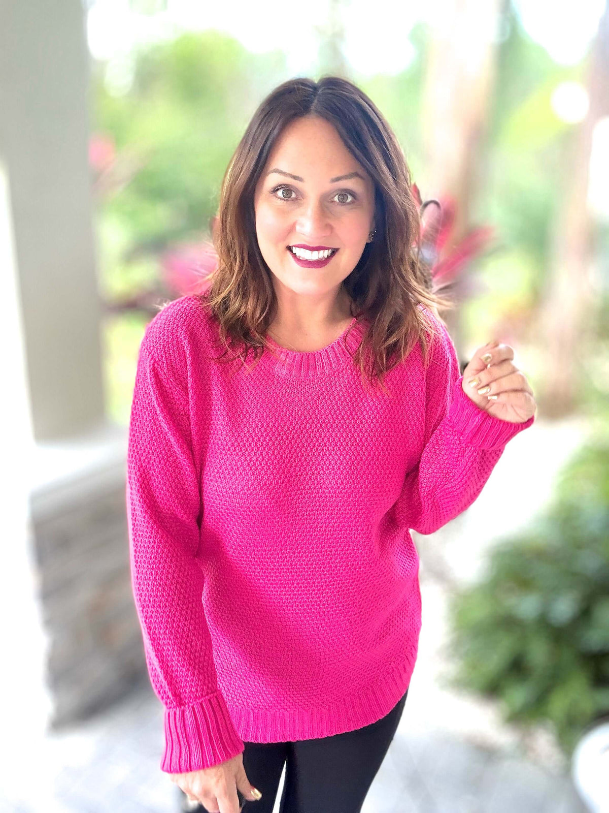 Woman wearing a vibrant pink sweater with a comfortable rounded bottom outdoors.