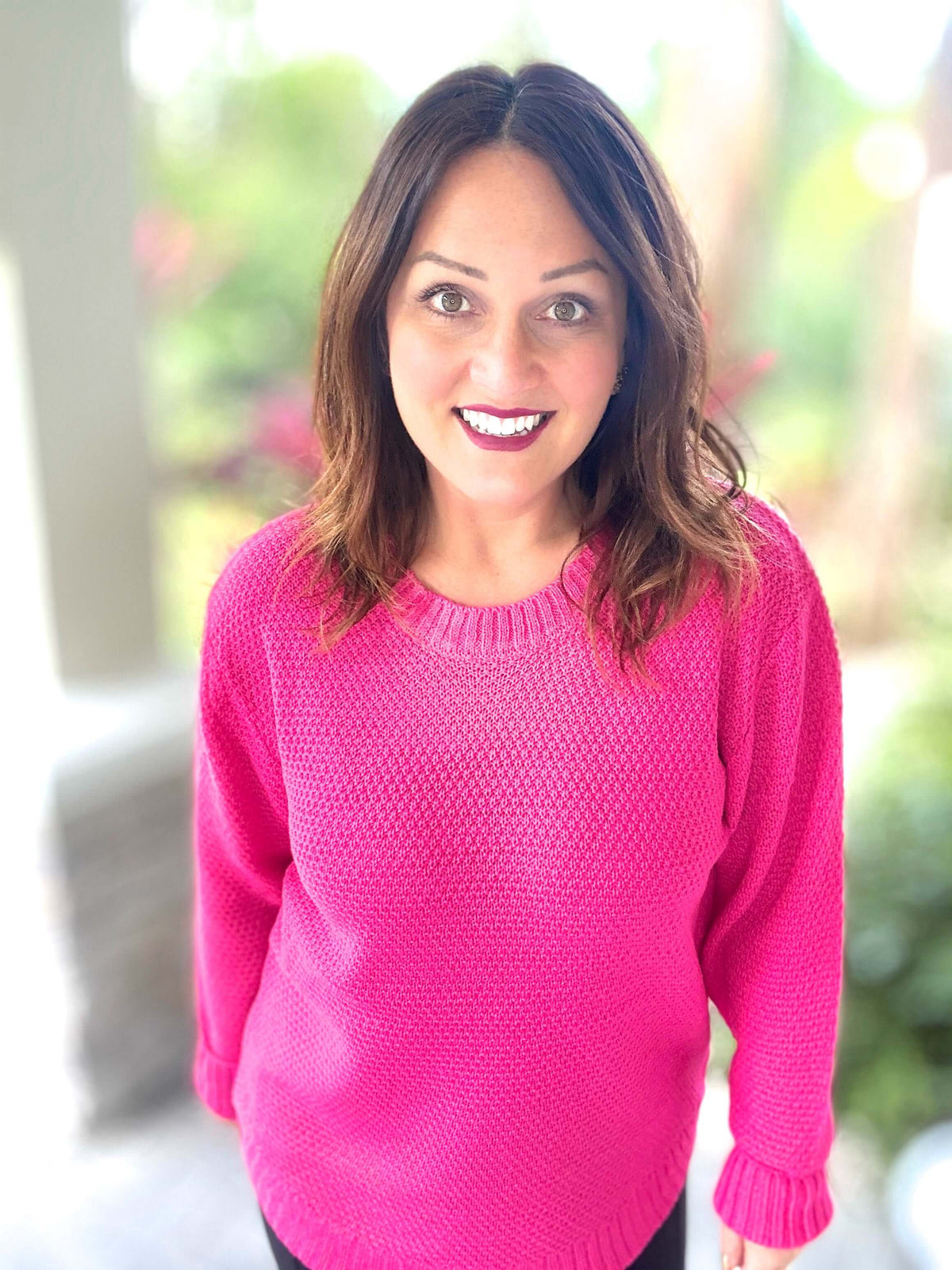 Woman wearing a bright pink Too Good to be Basic Sweater, standing outdoors.