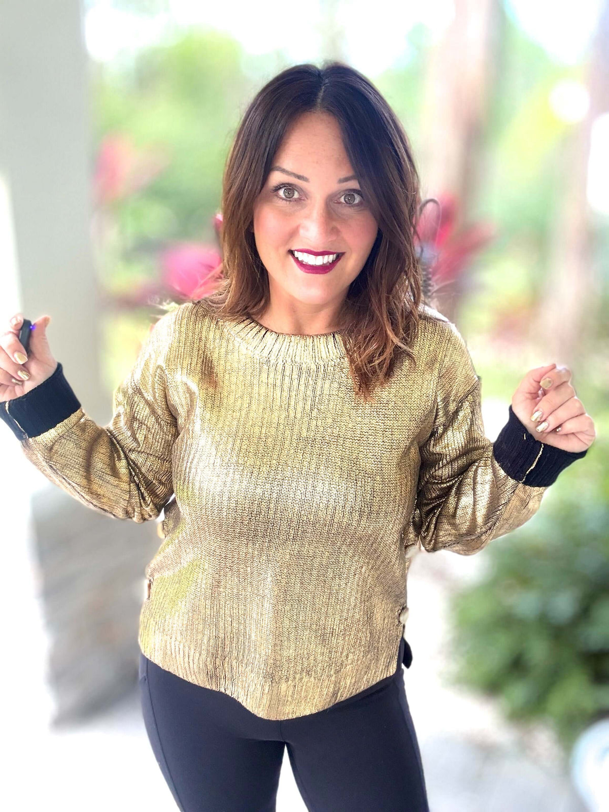 Woman wearing a black and gold metallic foil sweater with high low design, celebrating holiday style outdoors.