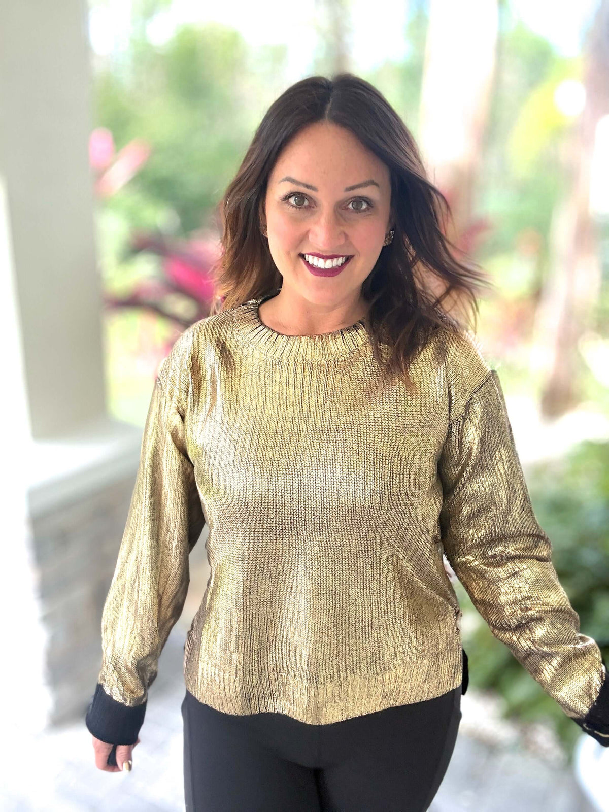 Woman wearing a festive metallic foil sweater, smiling outdoors.