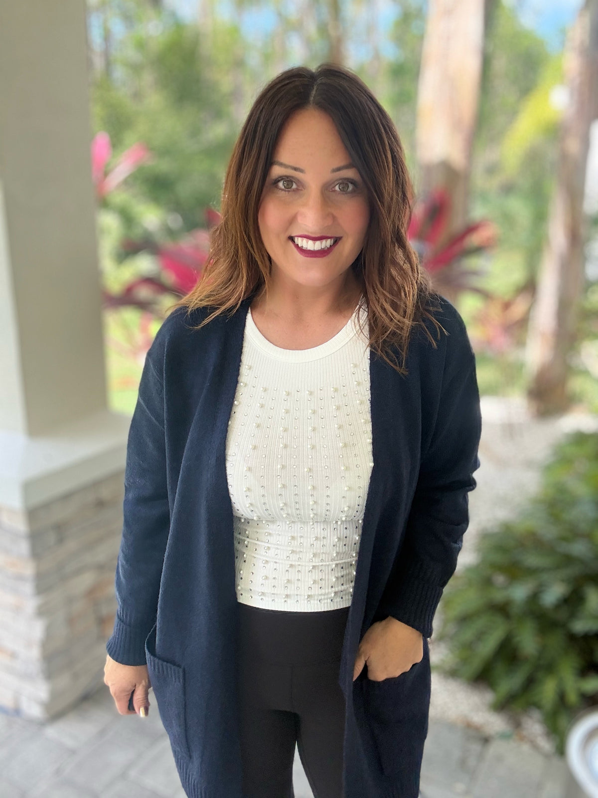 Woman wearing Autumn Moment Cardigan with front pockets, styled for cool weather, standing outside surrounded by greenery.