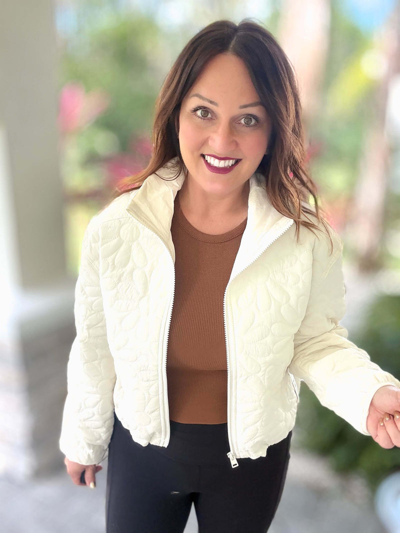 Woman wearing ivory floral quilted zip-up jacket, perfect for all weather, stylish and practical, comes with a storage bag.